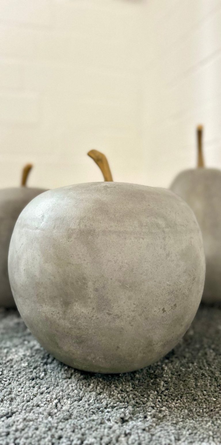 Wohnen auf Zeit Grau lackierte Äpfel aus Beton auf einem neutralen Hintergrund.