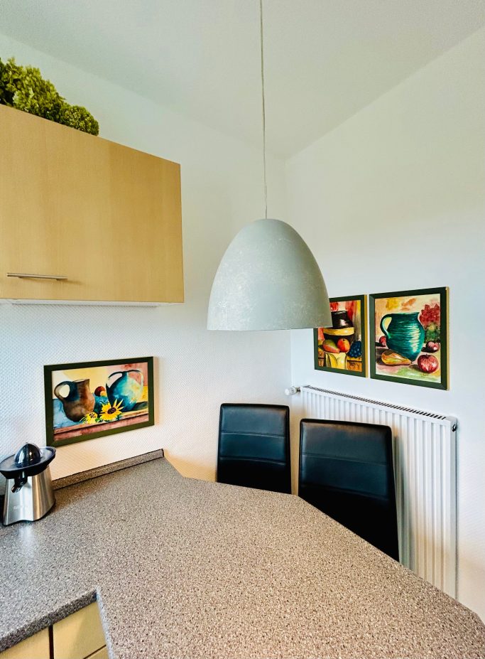 Küche Moderne Küche mit einem runden Lampenschirm, zwei Stühlen und bunten Wandbildern.