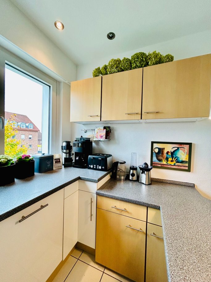 Küche 2 Moderne Küche mit hellem Holzschrank, Kaffeeautomat und Pflanzen auf der Fensterbank.