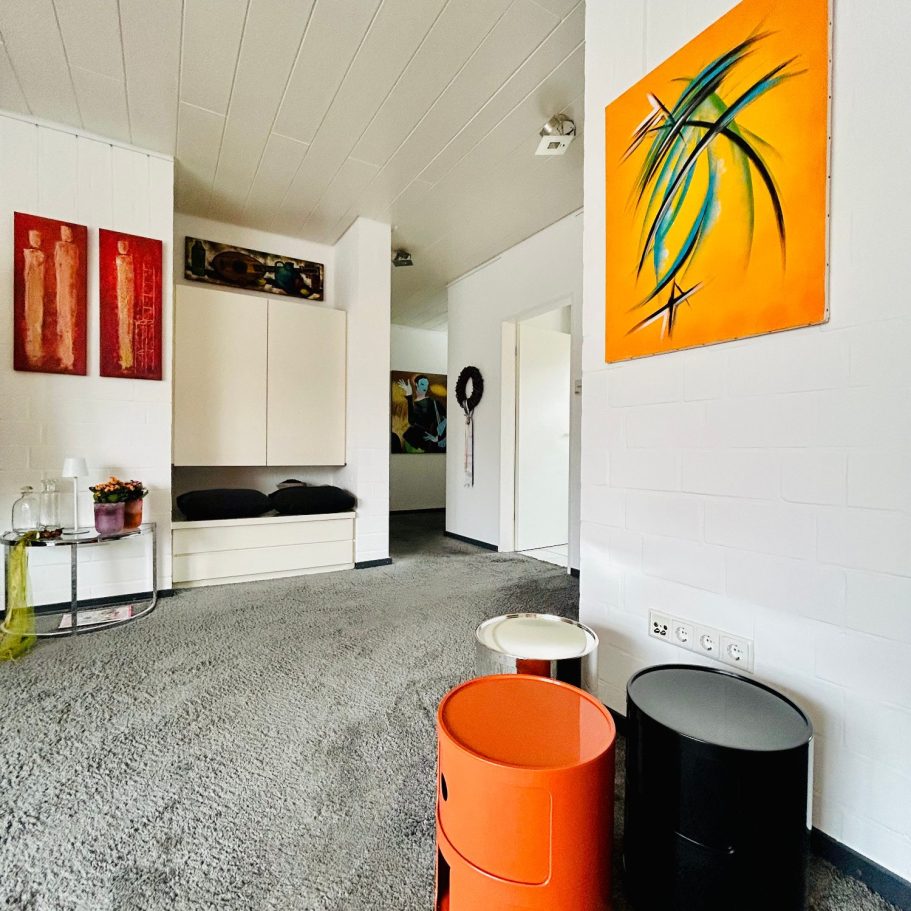 Luftiger KunstWohnRaum Heller Raum mit Teppich, bunten Aufbewahrungselementen und modernen Wandbildern.