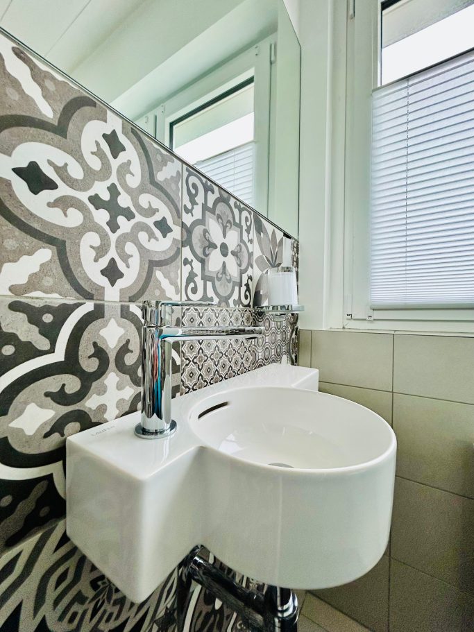 Toilette Weiße Wand mit modernem Waschbecken vor kunstvollem, gefliestem Hintergrund.