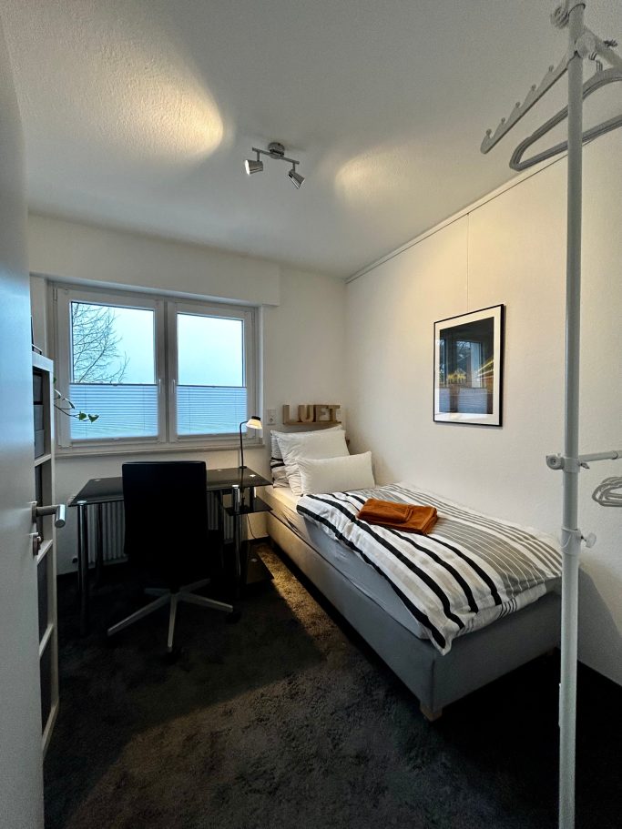 Einzelzimmer Kleines Zimmer mit Bett, Schreibtisch, Stuhl und Fenster mit Blick nach außen.