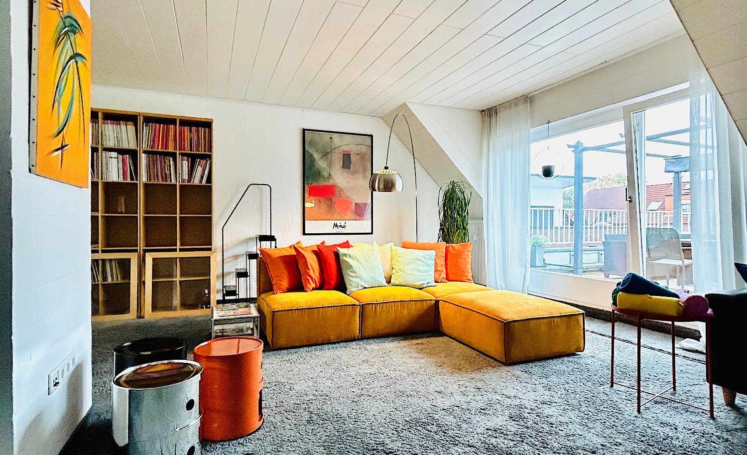 Wohnraum Helle Wohnlandschaft mit bunten Kissen, Bücherregal und großem Fenster.