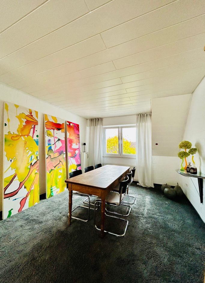 Wohnraum 3 Heller Raum mit bunten Gemälden, einem Holztisch und modernen Möbeln.