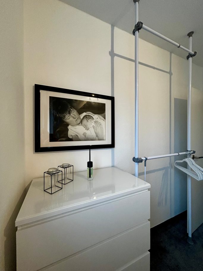 Zwei-Bett-Zimmer 2 Moderne Garderobe mit weißem Schrank, Bild an der Wand und minimalistischen Accessoires.