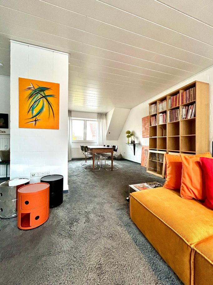 Wohnraum 2 Heller Wohnraum mit orangefarbenem Sofa, Bücherschrank und Tisch.
