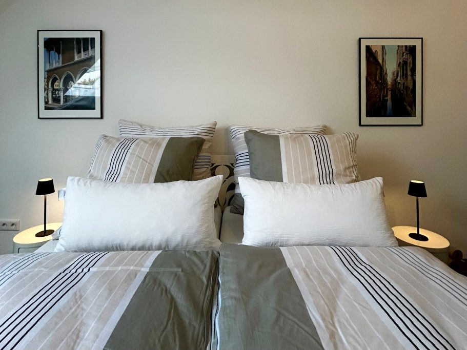 Familienzimmer Doppelbett mit gestreiften Bettwäsche, zwei Nachttischen und Bildern an der Wand.